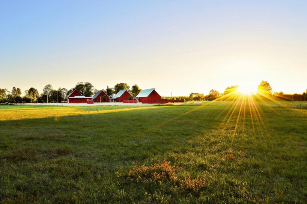 Sweden: Lagom (Not Too Much, Not Too Little) Beautiful sunset over a rural farm in Sweden with red barns and lush fields.