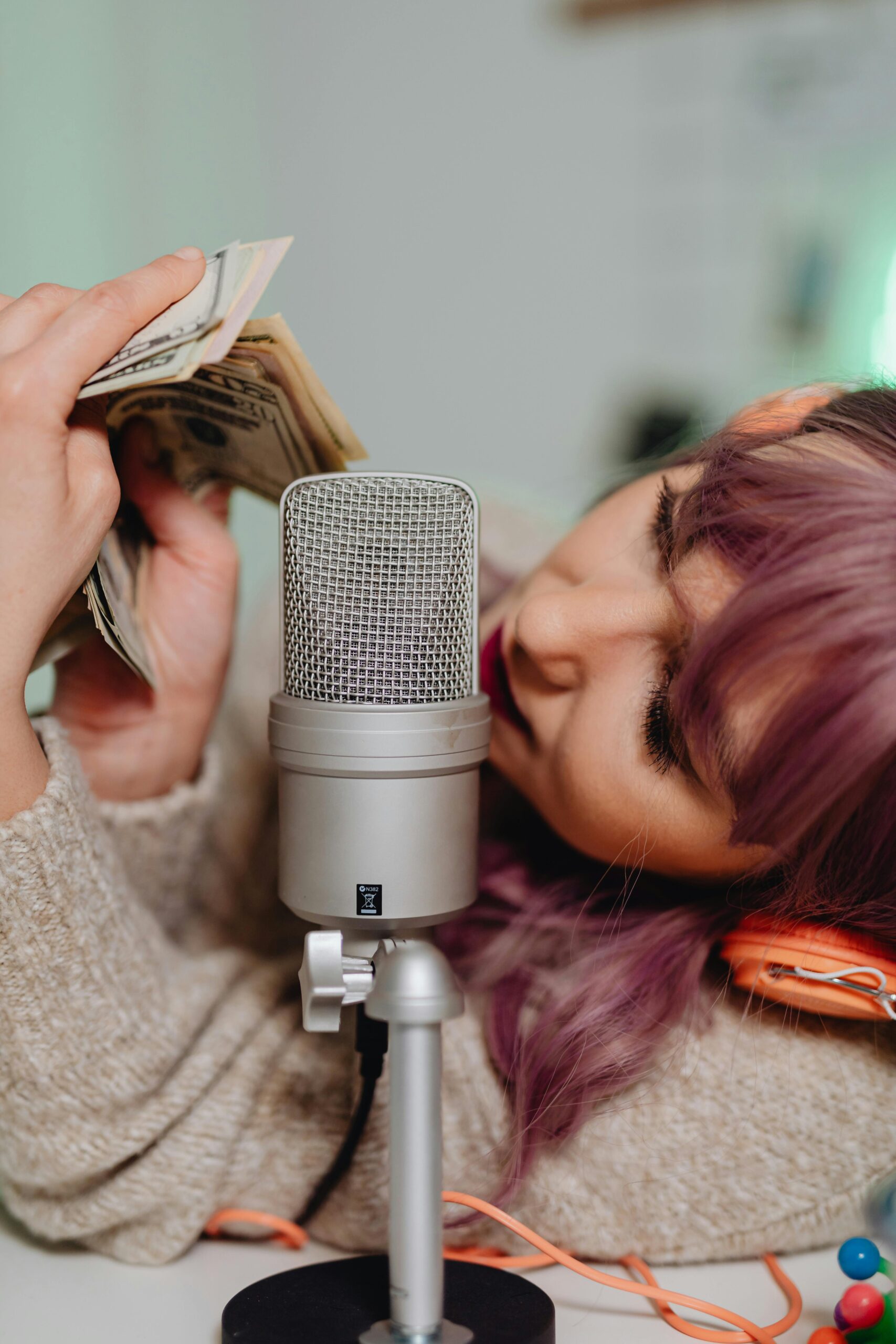 pexels photo 6920011 6920011 Young woman counts cash while holding a microphone for ASMR recording.